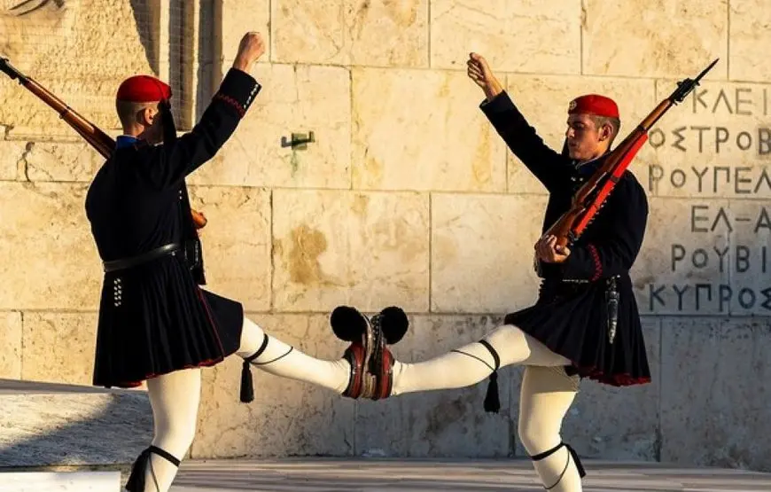 due-uomini-in-divisa-tradizionale-marciano-uno-di-fronte-all-altro-incrociando-le-gambe-e-alzando-una-mano-in-aria-indossano-delle-scarpe-particolari-un-basco-rosso-e-una-gonnella-nera-calza-bianche