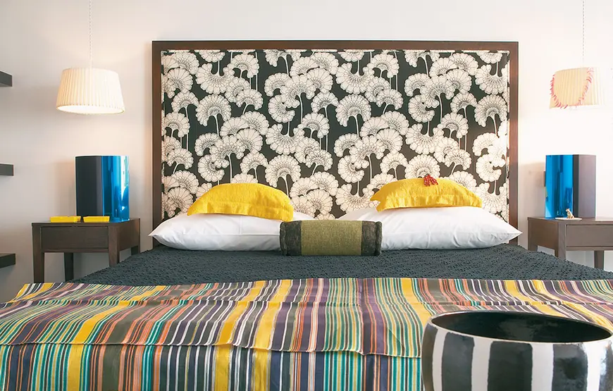 letto-matrimoniale-con-coperta-a-righe-colorate-cuscini-gialli-spalliera-con-disegni-bianchi-e-neri