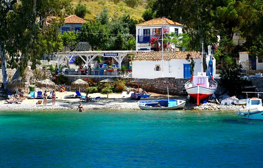 SPIAGGETTA-DAVANTI-A-UNA-TAVERNA-BIANCA-IL-MARE-TURCHESE-DAVANTI-ALCUNE-BARCHETTE-FERME-A-RIVA