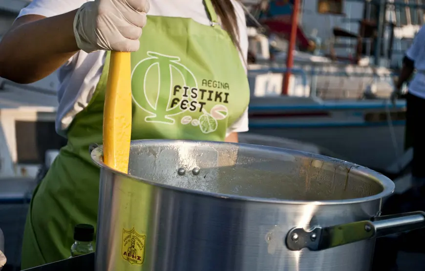 una-donna-con-il-grembiule-verde-con-scritto-fistiki-fest-mescola-qualcosa-in-un-pentolone