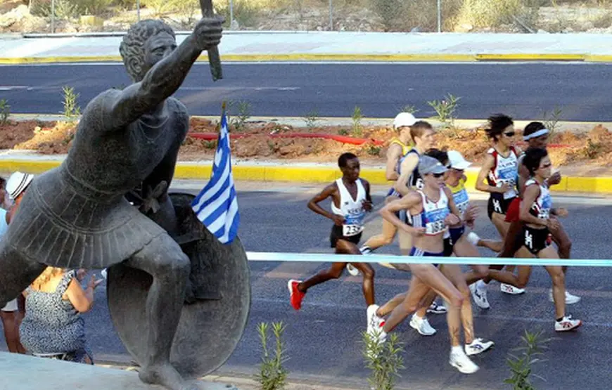 la-statua-di-filippide-il-primo-maratoneta-di-fianco-sulla-strada-moderni-maratoneti-durante-una-corsa