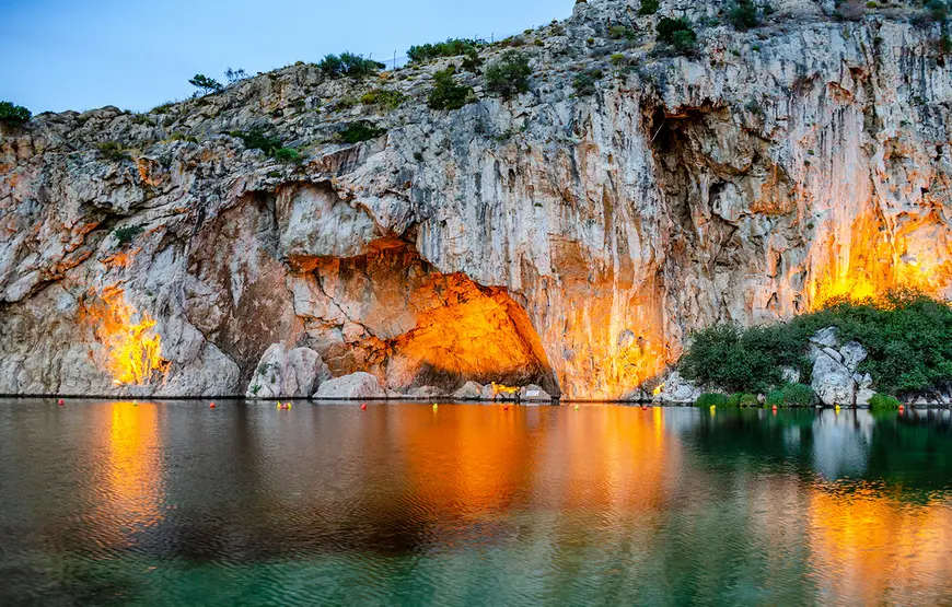 lago-in-cui-si-riflette-una-scogliera-alta-illuminata-con-luci-arancio