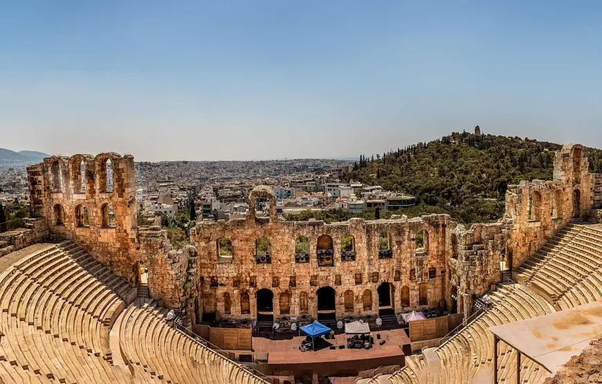odeon.di-erode-attico.una-scalinata.con-la-cavea-dietro-i-resti-del-teatro-ad-arcate-e-dietro-il-panorama-su-atene