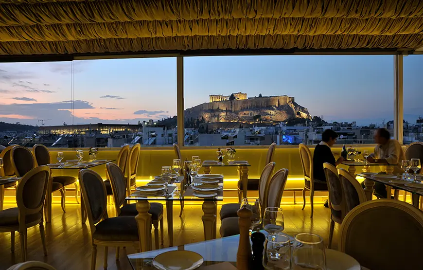 vista-di-atene-e-dell-acropoli-dal-ristorante-acropolian-spirit-hotel-di-atene-la-sala-è-illuminata-e-c-e-una-grande-vetrata