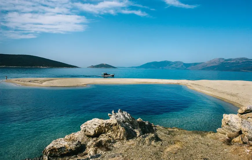 una-striscia-di-sabbia-si-inoltra-in-mare-turchese-creando-un-ansa-intorno-una-corolla-di-montagne-basse
