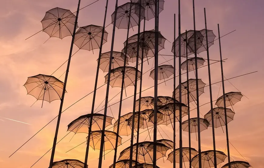 una sfilza di ombrellini trasparenti sono fissati a delle aste verticali, dieto un tramonto violaceo rosato