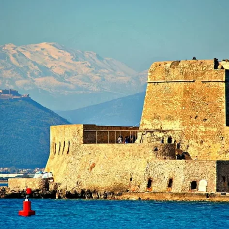 castello-di-nauplia-fortificato-davanti-al-mare-blu-dietro-il cielo-e-le-montagne-celesti