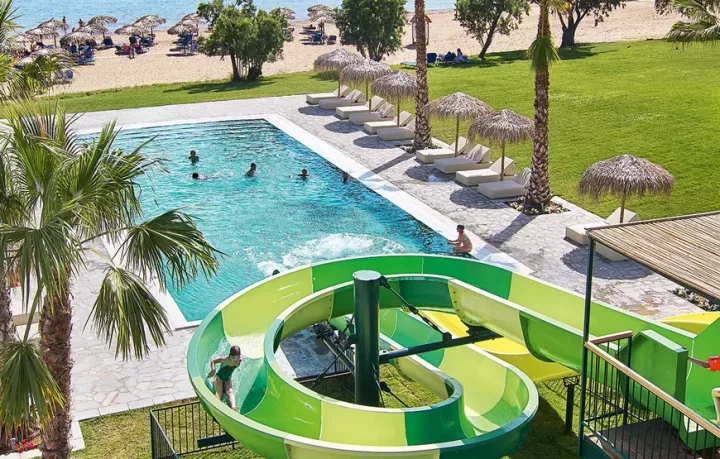 casa-marron-peloponneso-per-famiglie-grecoland uno-scivolo-di-una-piscina-a-forma-di-chiocciola-sotto-la-piscina-in-un-giardino-con-palme-e-ombrelloni
