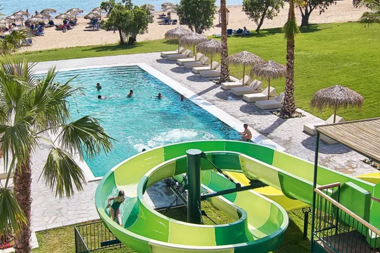 uno-scivolo-di-una-piscina-a-forma-di-chiocciola-sotto-la-piscina-in-un-giardino-con-palme-e-ombrelloni