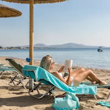 una-donna-è-sdraiata-al-sole-sulla-spiaggia-il-lettino-reclinato-legge-un-libro