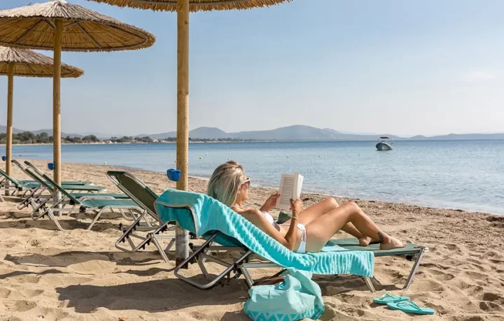 una-donna-è-sdraiata-al-sole-sulla-spiaggia-il-lettino-reclinato-legge-un-libro