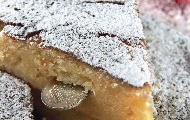 torta-vassilopita-con-zucchero-a-velo-sopra-una-fetta-da-cui-esce-una-monetina-tradizione-greca-per-il-capodanno