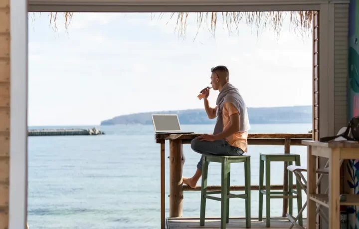 smart-working-in-grecia-vacanza-lavoro un-uomo-siede-su-uno-sgabello-in-un-lounge-bar-davanti-al-mare