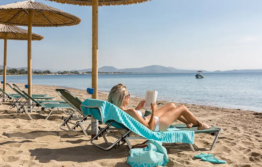 golden-coast-hotel-a-maratona-città una-donna-è-sdraiata-al-sole-sulla-spiaggia-il-lettino-reclinato-legge-un-libro