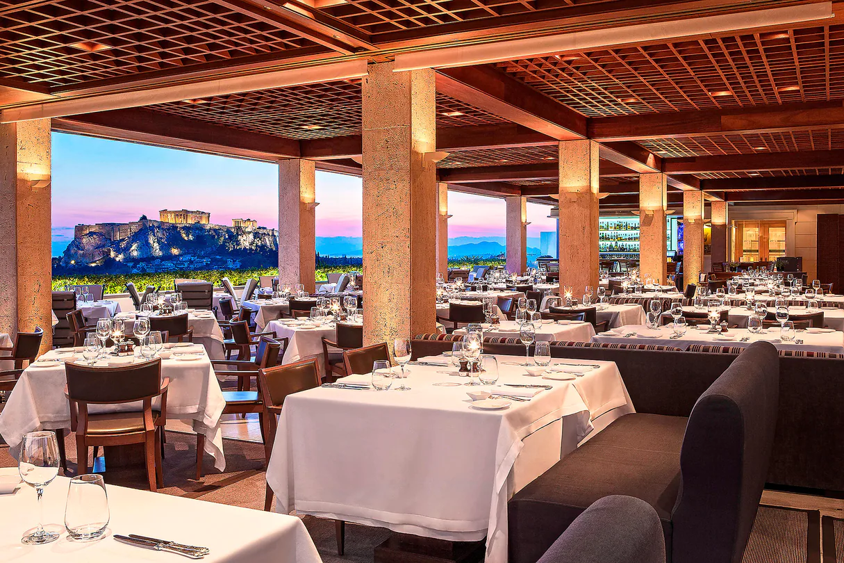 ristorante-con-tavoli-apparecchiati-sotto-una-struttura-di-legno-panoramica-con-acropoli-di-atene-illuminata